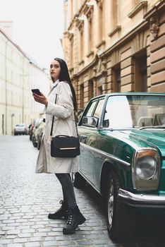 A woman on the street uses a mobile phone. online shopping. use of mobile applications. beautiful woman with long dark hair in a raincoat