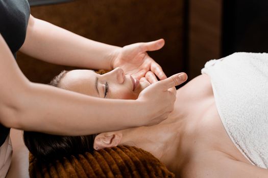 Facial massage close-up in spa center. Girl with perfect skin relaxing in massage room