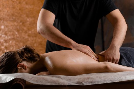 Attractive girl is relaxing on classic massage procedure in spa. Manual therapy. Masseur is doing back massage