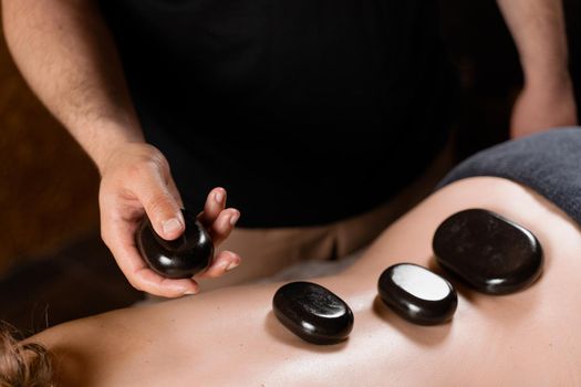 Heated stones on back of woman. Stone massage therapy in spa for relaxing