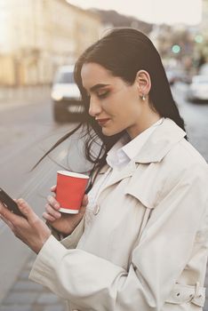 A woman on the street uses a mobile phone. online shopping. use of mobile applications. beautiful woman with long dark hair in a raincoat