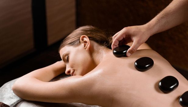 Masseur placed hot stone on the back of woman. Manual therapy in spa