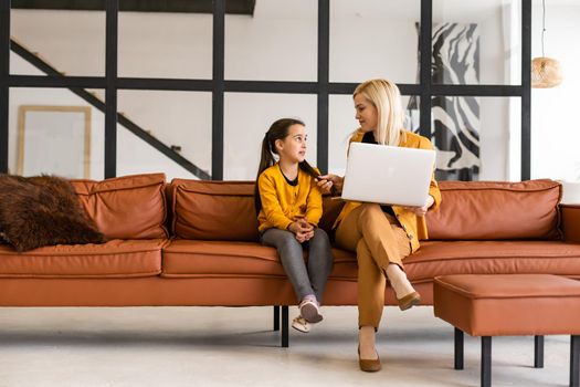 Online shopping or payments concept. Mother teaches his daughter using laptop at home. Sitting on the couch.