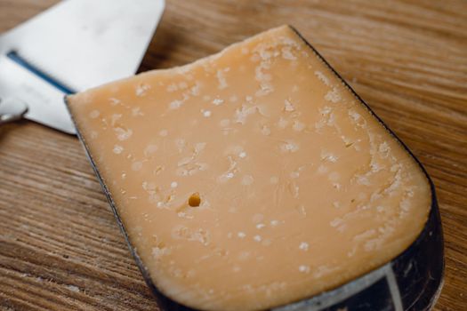 Parmesan hard aged cheese with slicer knife on wooden background. Snack tasty piece of cheese for appetizer