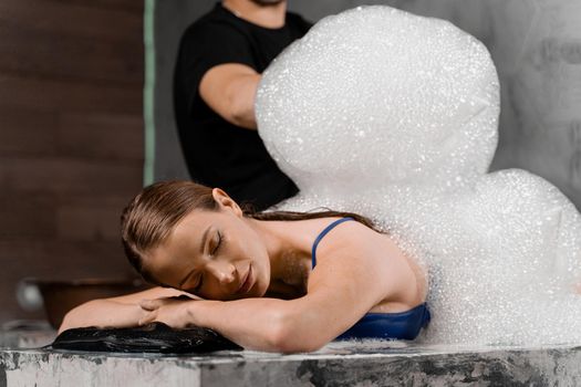 Attractive girl relaxing in spa. Masseur is making foam peeling in Turkish spa hammam