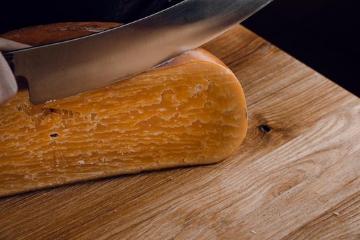 Slicing aged cheese parmesan with crystals using a cheesy dutch knife. Hard cheese with knife on dark background