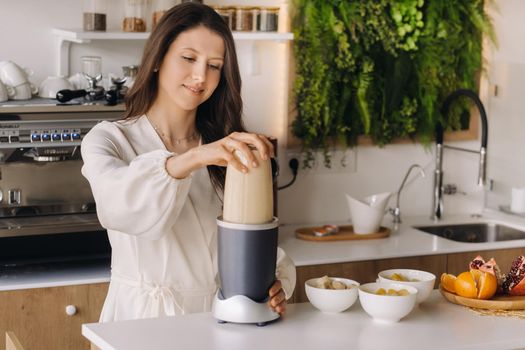 a girl makes a cocktail in a fruit blender in the kitchen. Diet for weight loss.