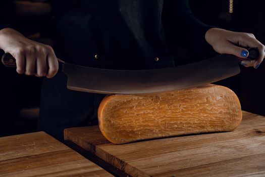 Slicing aged cheese parmesan with crystals using a cheesy dutch knife. Hard cheese with knife on dark background