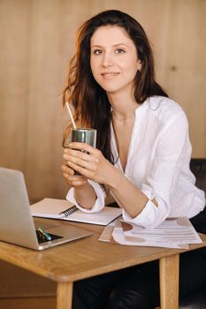 A young freelance woman with a cocktail in her hands at her workplace at work.