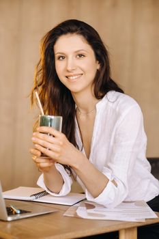 A young freelance woman with a cocktail in her hands at her workplace at work.