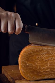 Close-up slicing aged cheese parmesan with crystals using a cheesy dutch knife. Hard cheese with knife