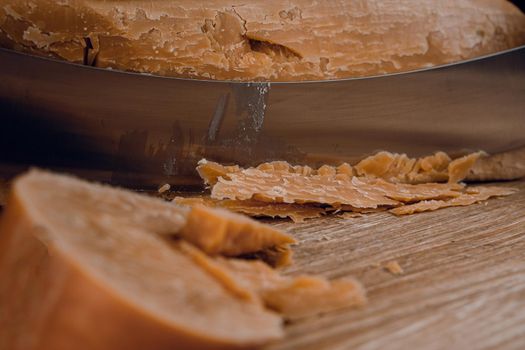 Slicing aged cheese parmesan with crystals using a cheesy dutch knife. Hard cheese with knife on dark background