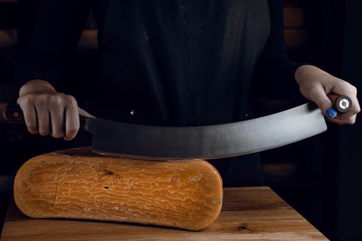 Slicing aged cheese parmesan with crystals using a cheesy dutch knife. Hard cheese with knife on dark background