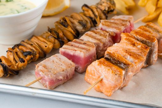 Barbecue seafood kebab with grilled mussels, tuna, salmon on a wooden skewer with white sauce and lemon