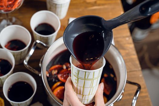 Red mulled hot and spiced wine alcohol drink pouring into disposabla glass. Grog with cinnamon seasonal christmas drink