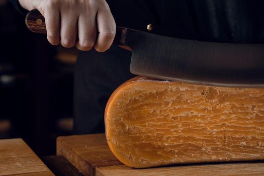 Close-up slicing aged cheese parmesan with crystals using a cheesy dutch knife. Hard cheese with knife