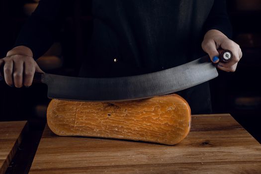 Slicing aged cheese parmesan with crystals using a cheesy dutch knife. Hard cheese with knife on dark background