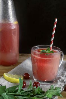 Fresh watermelon juice with cherries and lemon in a glass. Slices of watermelon and cherry berries on the table. Front view. Copy space. The concept of natural nutrition.