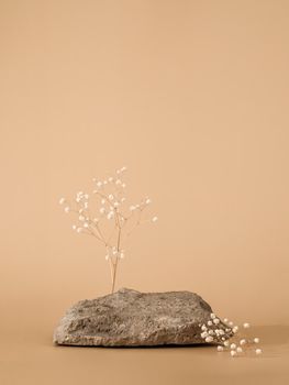 Mockup geometric shape podium. Stone shape with gypsophila flowers over pastel beige background. Can use as perfume and cosmetic mock up. Copy space. Vertical. Natural rock podium