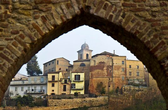 The buildings of Ripatransone in the Marche region of Italy are seen through a stone arch