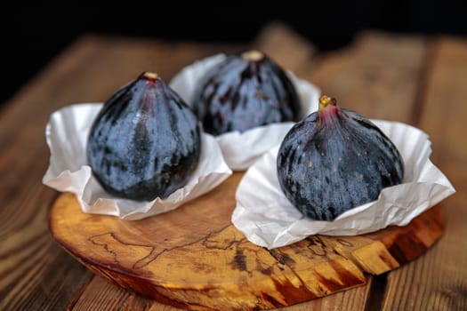 Fresh purple figs are wrapped in paper, on a wooden background from old boards. Raw exotic figs. Low key