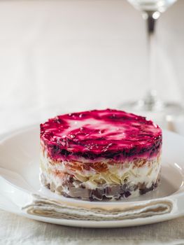 Layered salad herring under fur coat on table. Portion of traditional russian salad with herring, beet and other vegetables on white linen tablecloth. Copy space. Vertical.