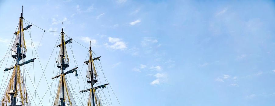 The masts of the old ship on the background of the blue sky. The concept of travel Copy space and banner