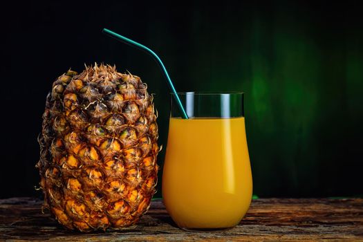 Fresh pineapple juice in a glass and fresh pineapple on a dark green background.