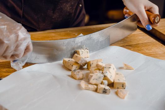 Slicing blue cheese dorblu, gorgonzola, roquefort. French gourmet traditional cuisine. Mix of cheeses on plate