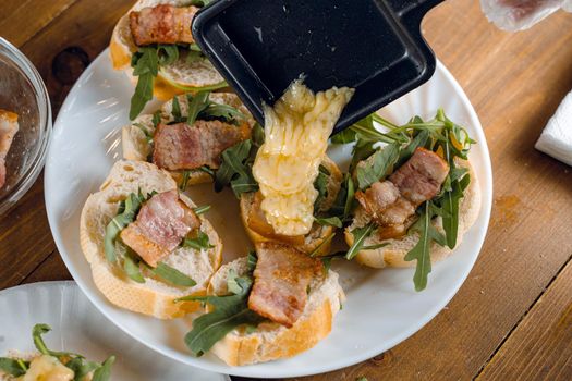 Raclette melted cheese for sandwich with fried bacon and arugula traditional french cuisine. Plate with snacks