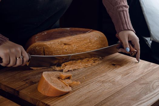 Slicing aged cheese parmesan with crystals using a cheesy dutch knife. Hard cheese with knife on dark background