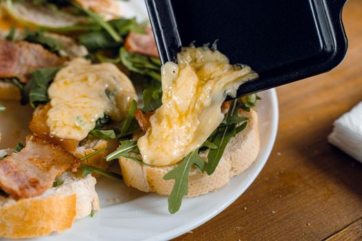 Raclette melted cheese for sandwich with fried bacon and arugula traditional french cuisine. Plate with snacks