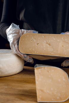 Holding goat cheese wheel and big pieces of it. Mix of cheeses from goat milk.