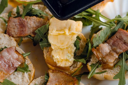 Raclette melted cheese for sandwich with fried bacon and arugula traditional french cuisine. Plate with snacks