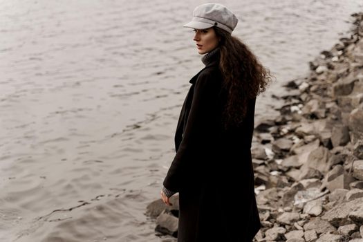 Girl with curly hair on the background of birch with stones and lake in autumn.