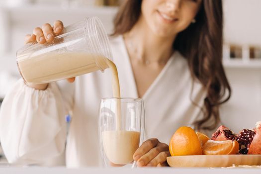 Close-up of a girl's hands pouring a fresh fruit cocktail of bananas and an orange in the kitchen. Diet for weight loss.