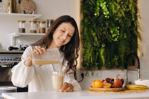 Smiling girl pours a fresh fruit cocktail of bananas and orange in the kitchen. Diet for weight loss.