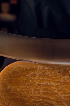 Close-up slicing aged cheese parmesan with crystals using a cheesy dutch knife. Hard cheese with knife