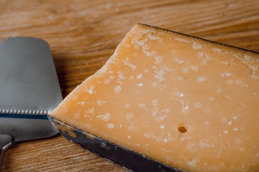 Parmesan hard aged cheese with slicer knife on wooden background. Snack tasty piece of cheese for appetizer