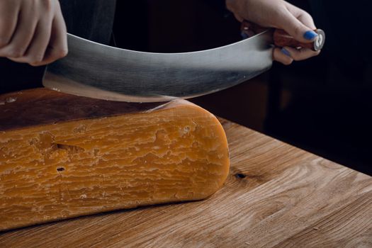 Slicing aged cheese parmesan with crystals using a cheesy dutch knife. Hard cheese with knife on dark background