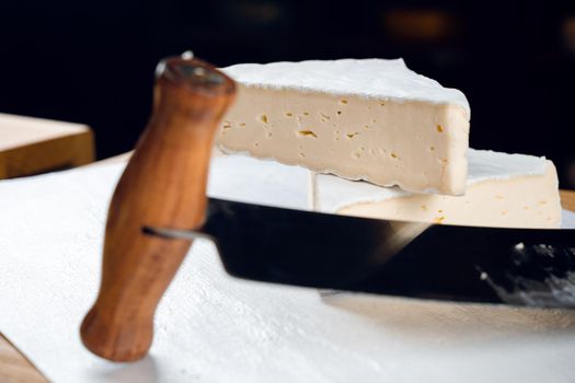 Brie soft white cheese from cow milk. Slicing brie on the wooden table. Organic delicious food