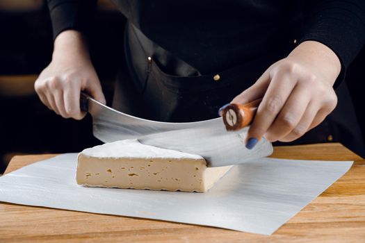 Brie soft white cheese from cow milk. Slicing brie on the wooden table. Organic delicious food