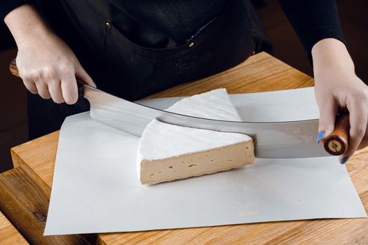 Brie soft white cheese from cow milk. Slicing brie on the wooden table. Organic delicious food