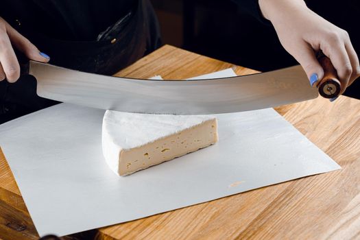 Brie soft white cheese from cow milk. Slicing brie on the wooden table. Organic delicious food