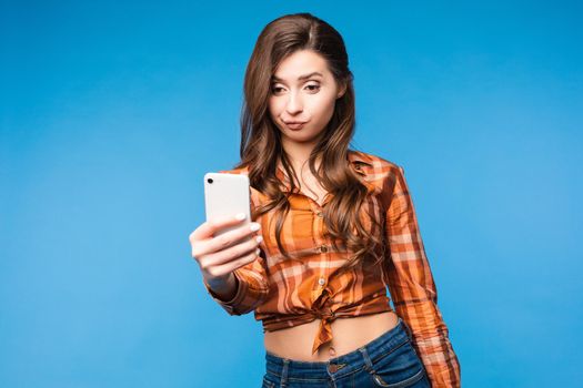 Full length portrait of happy stylish woman with charming smile in fashion sweater and brown skirt. She is standing and taking selfie with smartphone. Isolated on gray background