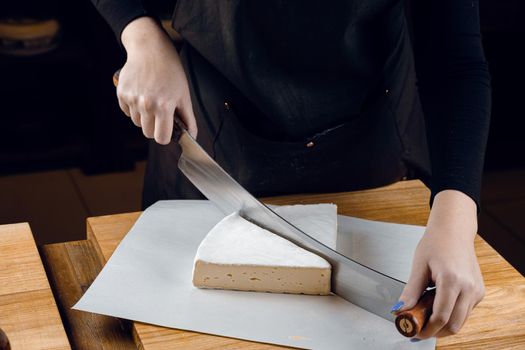 Brie soft white cheese from cow milk. Slicing brie on the wooden table. Organic delicious food