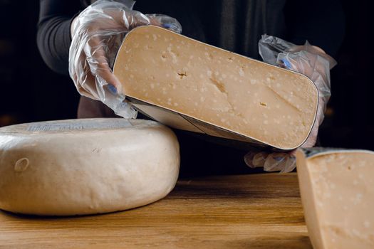 Holding goat cheese wheel and big pieces of it. Mix of cheeses from goat milk.