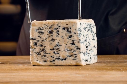 String for slicing blue cheese. Mix of cheeses on plate. Slicing dorblu, gorgonzola, roquefort. French gourmet cuisine