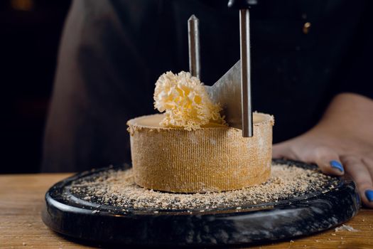 Shaving tete de moine cheese using girolle knife. Monks head. Variety of Swiss semi-hard cheese made from cows milk.