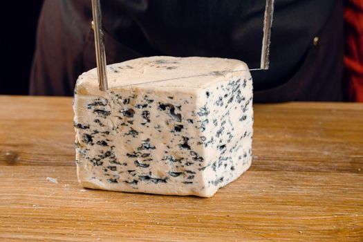 String for slicing blue cheese. Mix of cheeses on plate. Slicing dorblu, gorgonzola, roquefort. French gourmet cuisine